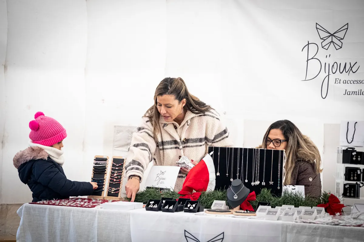 Une enfant en bonnet rose choisit un bracelet sur un stand de bijoux