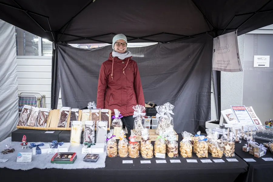 Une artisane derrière son stand de biscuits et de chocolats de Noël